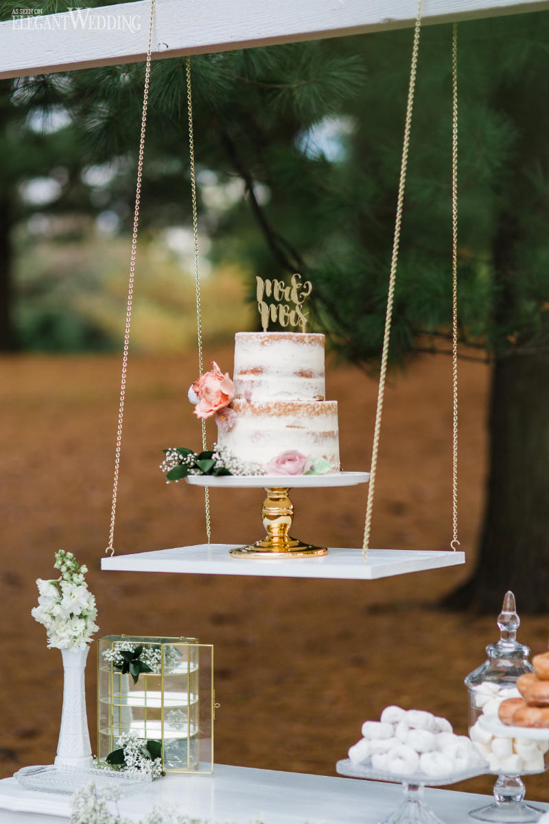 Semi naked cake with thin white frosting, gold laser cut cake topper and minimal floral decoration on an elegant hanging swing display. // Jaw-dropping suspended cake display ideas for your wedding day. // mysweetengagement.com