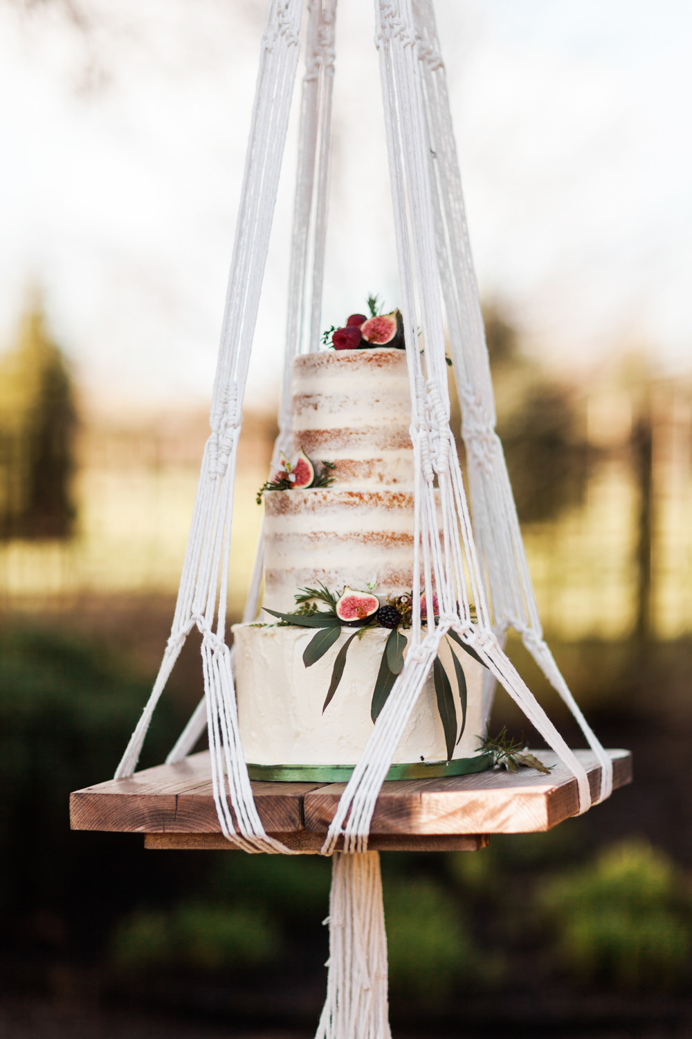 Boho vibes with this semi-naked fig wedding cake on a macramé hanging swing. // Jaw-dropping suspended cake display ideas for your wedding day. // mysweetengagement.com