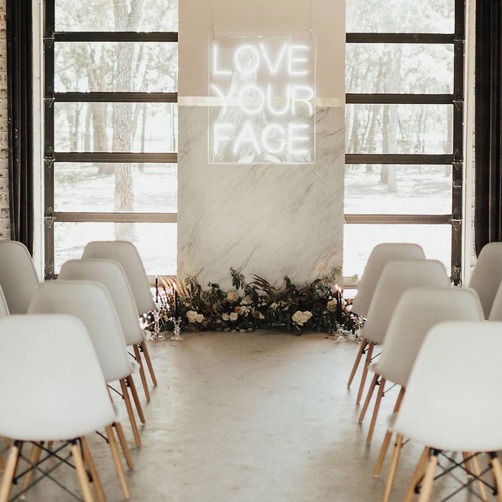 This minimalist and modern all white indoor wedding ceremony has just the right amount of fun with this unexpected "Love your face" neon sign on the backdrop. // Fun and bright neon wedding sign decor ideas // mysweetengagement.com
