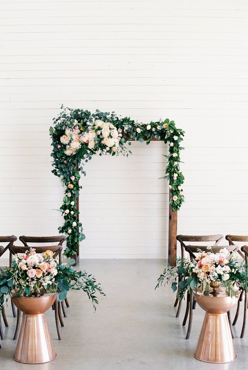 This all white wedding ceremony venue with dark wood arch and chairs, combined with copper accents and peach flowers looks an incredible mix between rustic and chic. // ❤ Check Out These Gorgeous 20 Indoor Wedding Ceremony Ideas. // http://mysweetengagement.com/indoor-wedding-ceremony-ideas