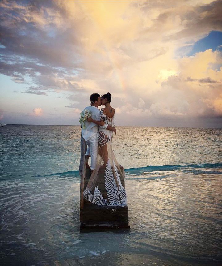 Isabeli Fontana and Di Ferrero pose kissing in front of the ocean with a rainbow on the background