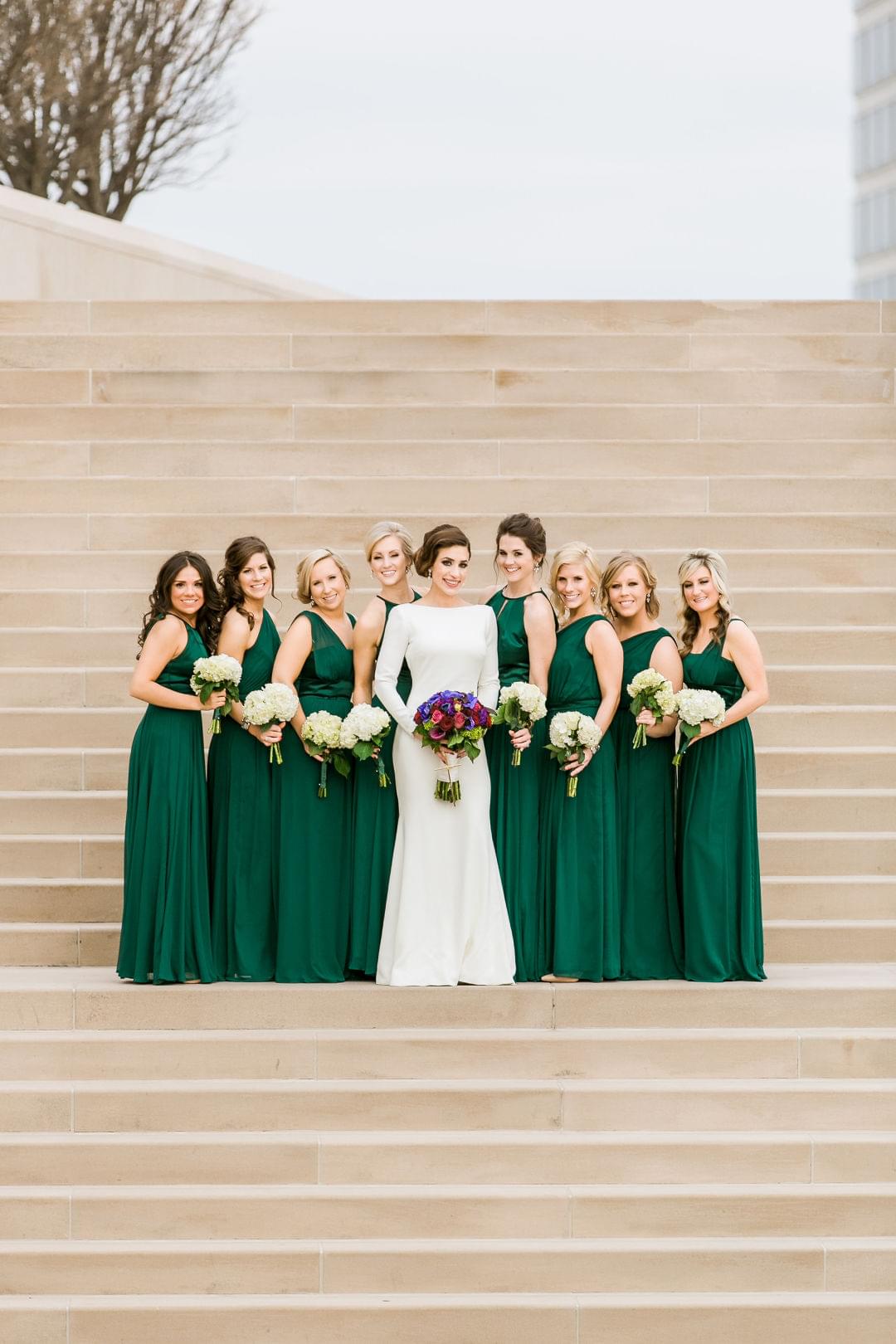  bride wearing a long sleeve dress and bridesmaids long emerald green dresses