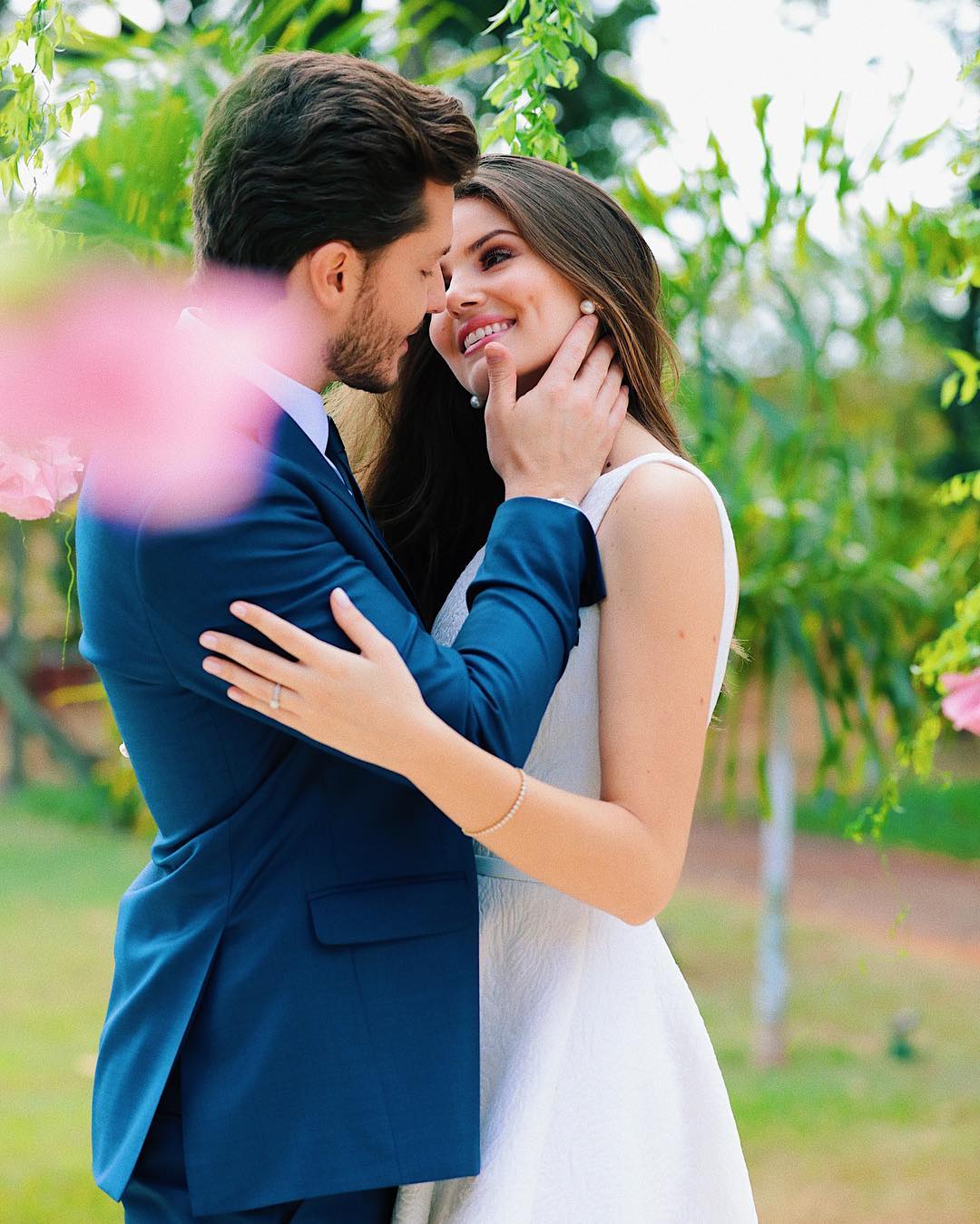 Romantic couple pose idea for a portrait. The groom is rocking an elegant navy blue suit and the bride a stunning mid length white dress with embroidered flowers. // ❤️This civil Wedding is absolutely delightful (Camila Queiroz and Kleber Toledo I Do's) // https://mysweetengagement.com/mid-length-civil-wedding-dress/