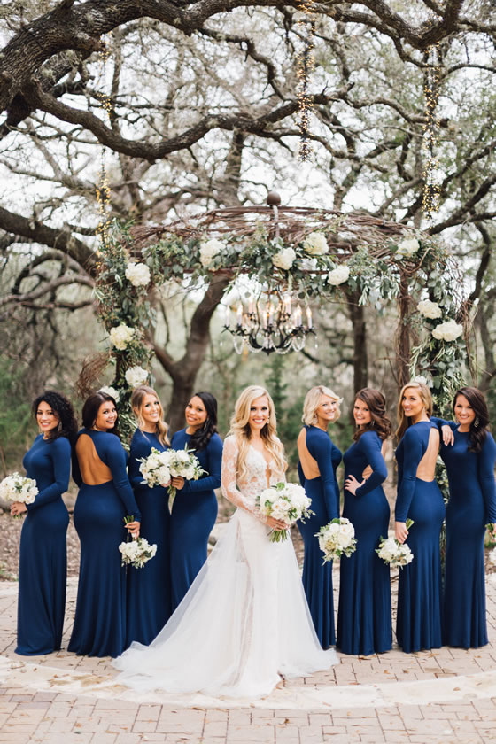 Long sleeve sexy open back navy blue bridesmaid dress inspiration. Perfect for a winter wedding. Bridesmaids and bride have an all white bouquet with matching flowers on the ceremony decor.