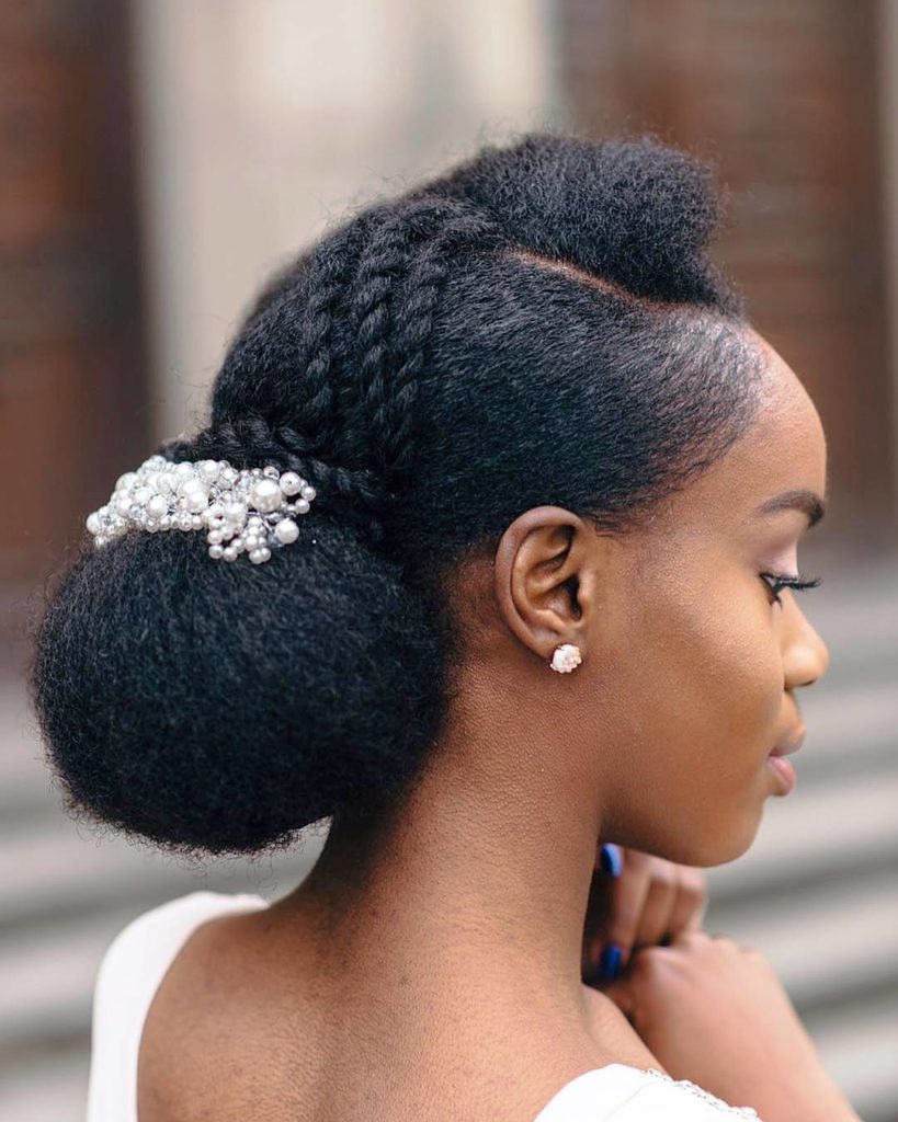 Gorgeous black bride with an elegant low bun, embellished by small braids and a chic hairpiece.