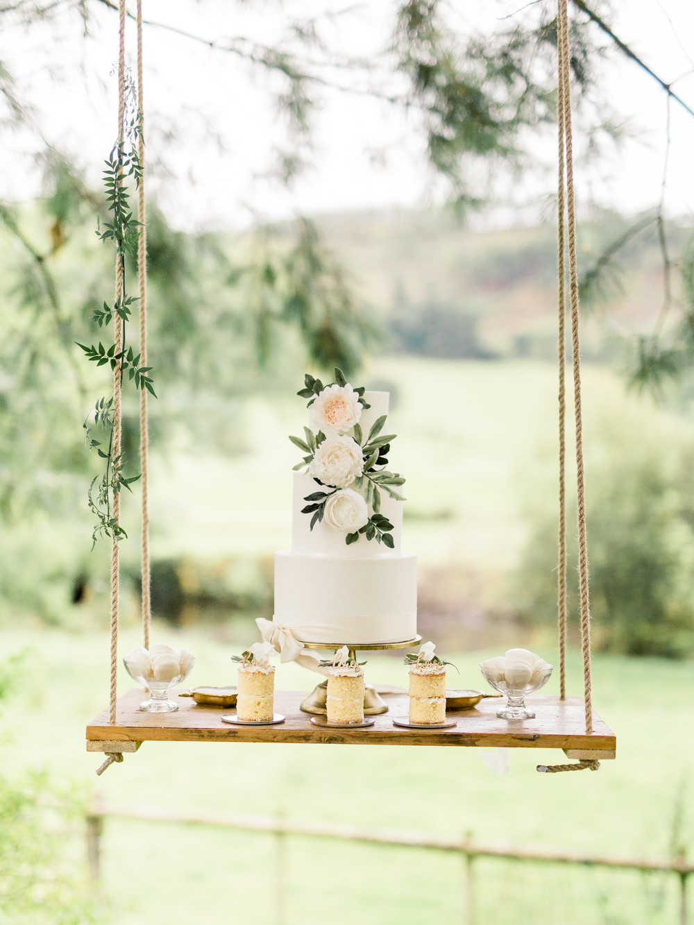 This minimalist all white wedding cake embellished with some greenery on a hanging swing is everything! // Jaw-dropping suspended cake display ideas for your wedding day. // mysweetengagement.com