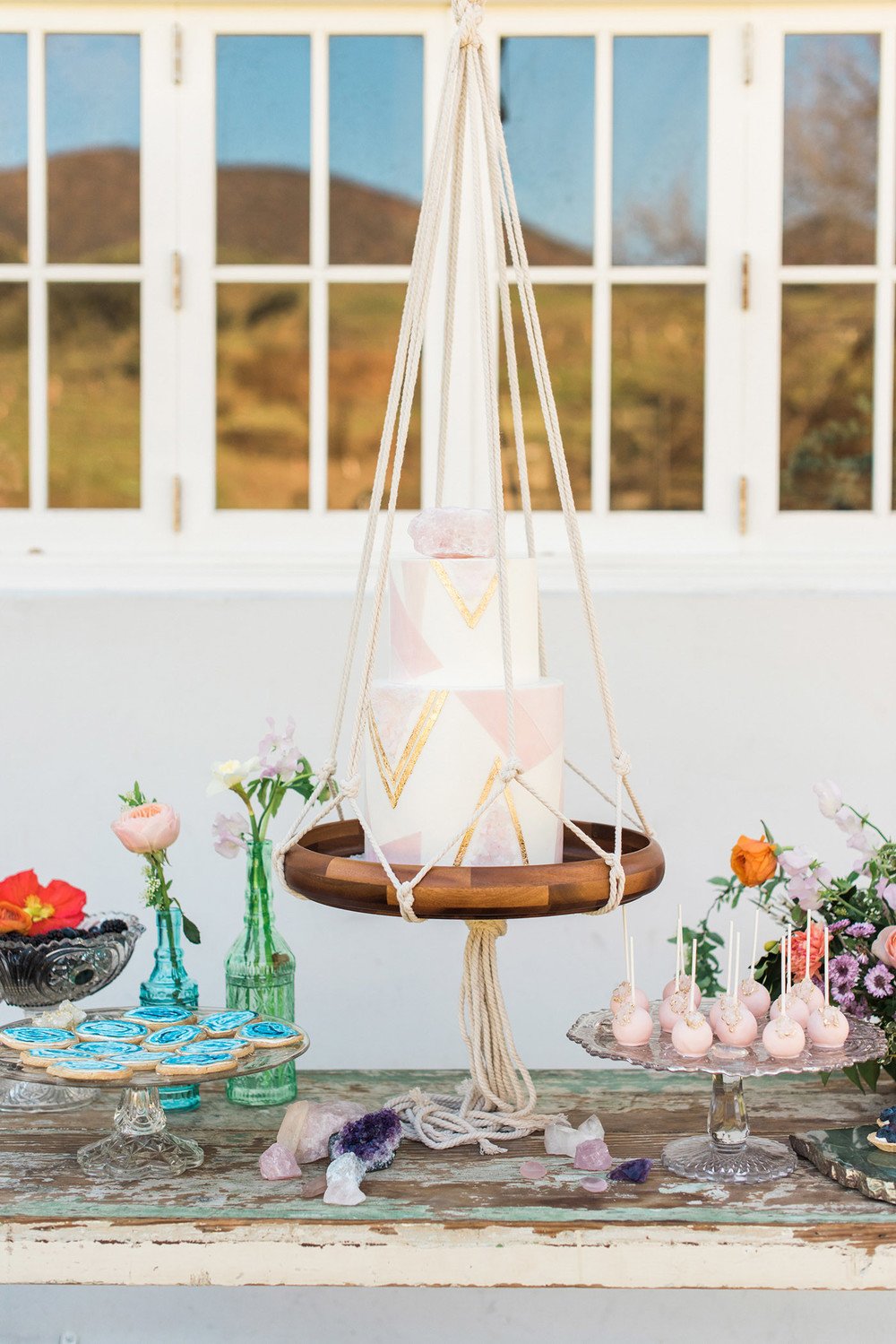 Boho meets modern. Minimalist wedding cake with geometric triangles pattern on a hanging macramé swing with circular shaped wood base. // Jaw-dropping suspended cake display ideas for your wedding day. // mysweetengagement.com