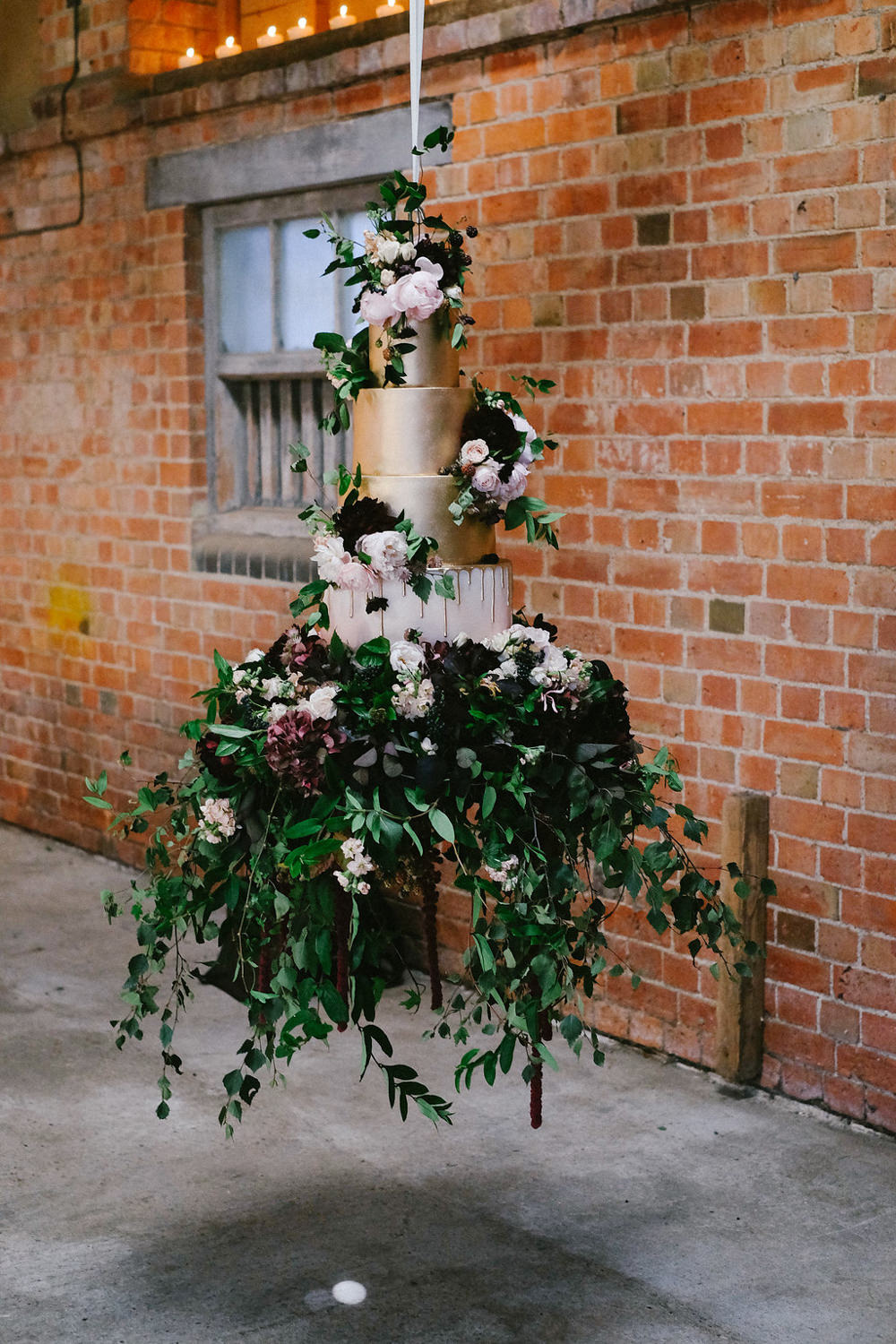 Say YES to this dramatic floating cake display. Warm gold frosting with blush and dark red flowers and a huge greenery skirt. // Jaw-dropping suspended cake display ideas for your wedding day. // mysweetengagement.com
