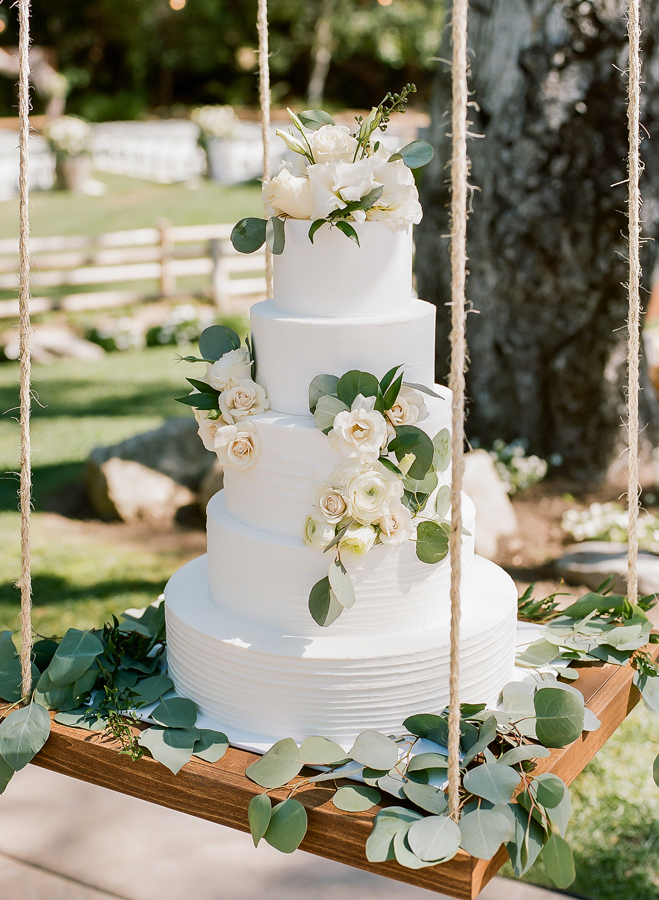 All white wedding cake, embellished with white flowers and greenery eucalyptus on a hanging swing display. // Jaw-dropping suspended cake display ideas for your wedding day. // mysweetengagement.com