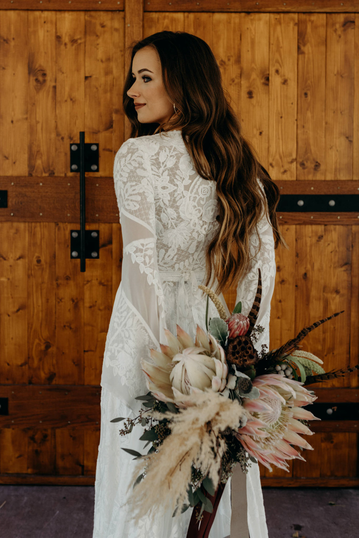Boho style wedding dress with long sleeve. Bride with long hair down and king protea and pampas grass bouquet.