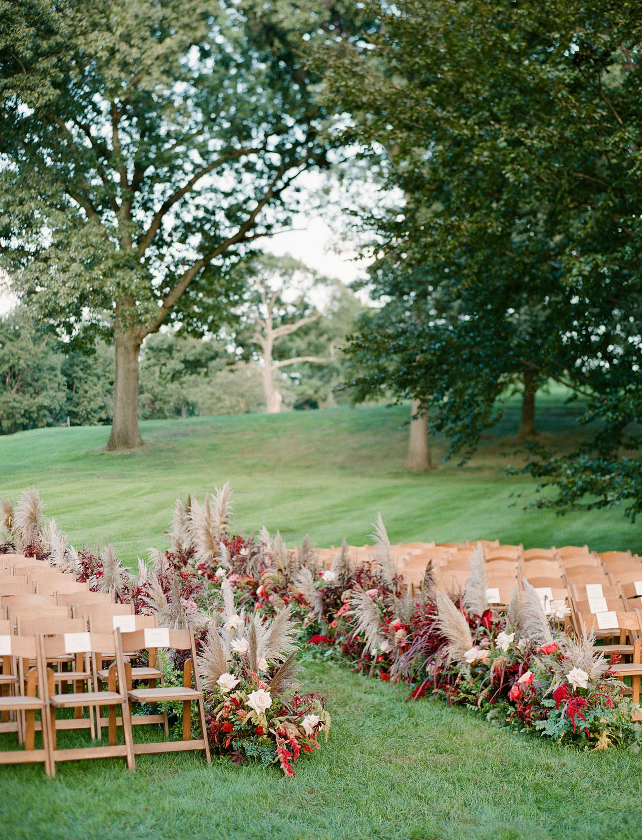 Garden wedding ceremony with wood chairs and pampas grass and red flowers aisle decor