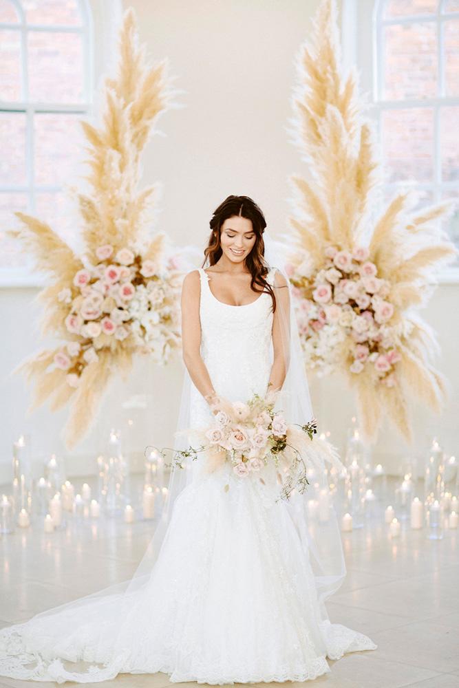 Indoor wedding ceremony decoration with high pampas grass background and lots of white candles on the floor