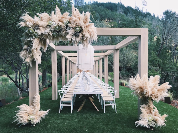 wedding reception long table with white color decorations featuring large pampas grass