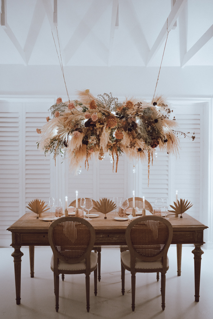 Minimal indoor table decoration with earth tone elements and hanging pampas grass and floral installation.