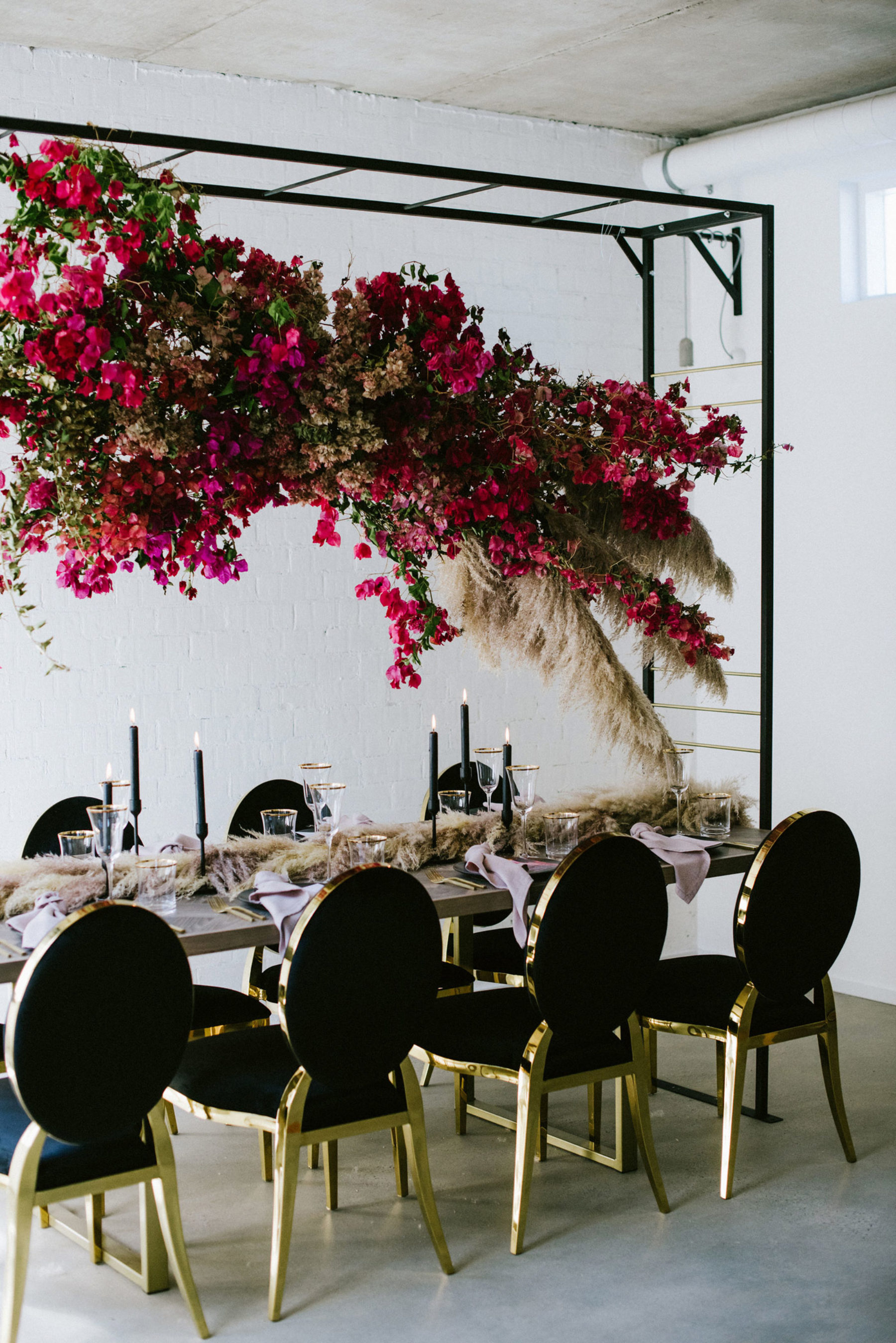 Black and gold wedding reception table decor with hanging red flowers and pampas grass.