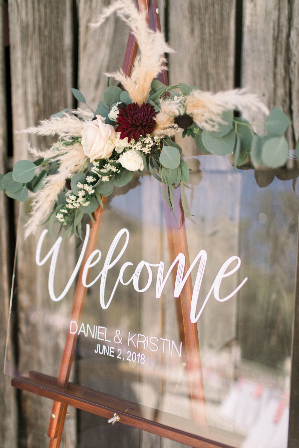 Acrylic wedding welcome sign embellished with Cortaderia Selloana, greeneries and white and burgundy florals.
