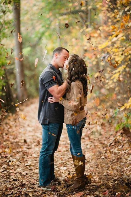 engagement photo of a couple kissing with fall leaves in the air 