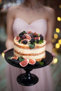 small naked wedding cake topped with blackberries and figs on a black cake stand