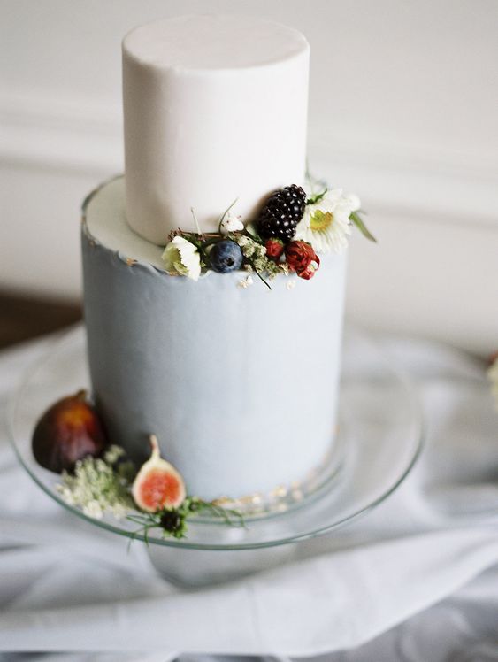 two tiered gray and white frosting wedding cake decorated with dark fruits and minimal flowers