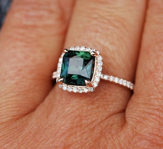emerald green gemstone engagement ring with gold metal setting surrounded with pave diamonds