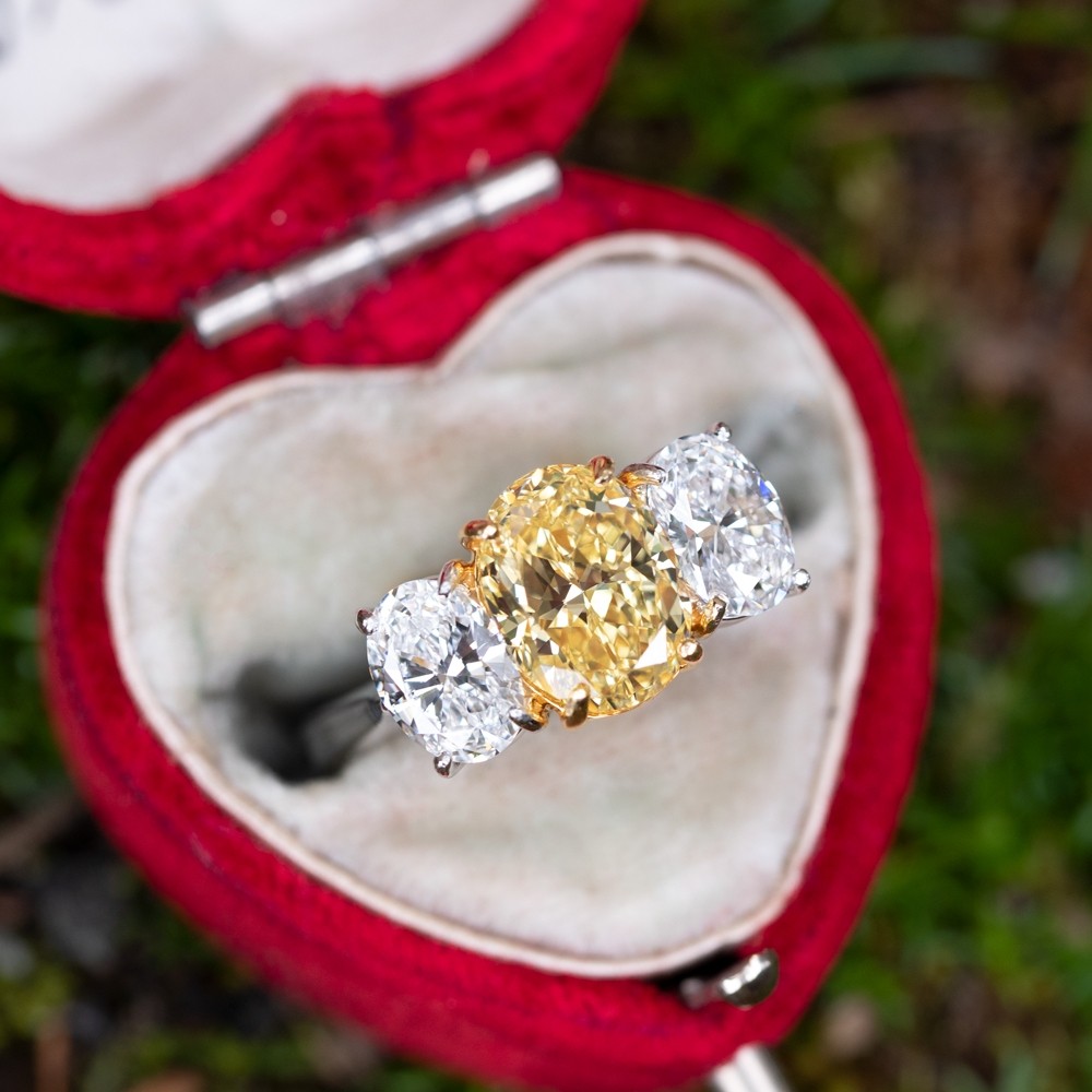 3 oval shaped engagement ring with center diamond on yellow diamond on a heart shaped ring box