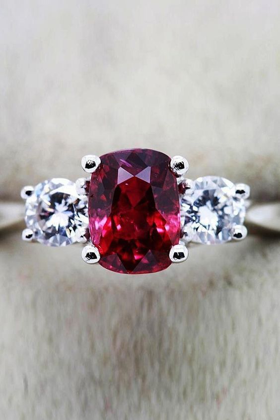 3 stone engagement ring with a center oval shaped ruby gemstone and two side round diamonds