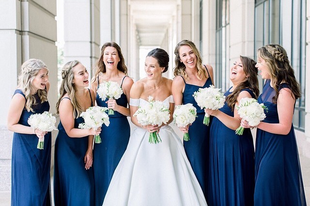 elegant bride and bridesmaids who wear navy dresses and hold all white bouquets