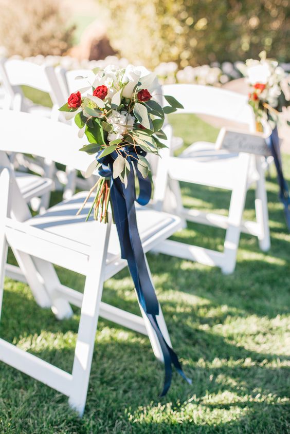 white ceremony chairs embellished with flowers and navy blue ribbon