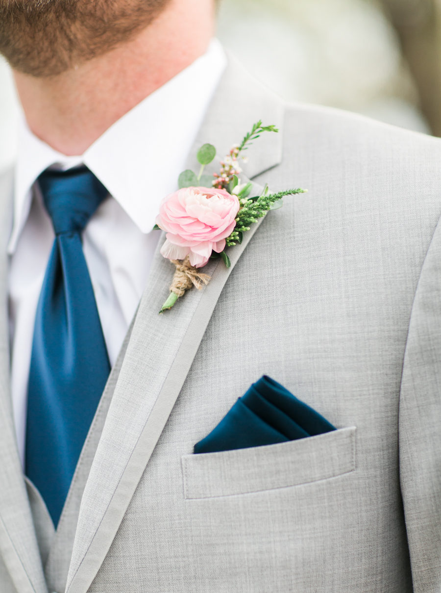 groom wearing gray suit with a blush pink boutonnière and navy blue tie and pocket square