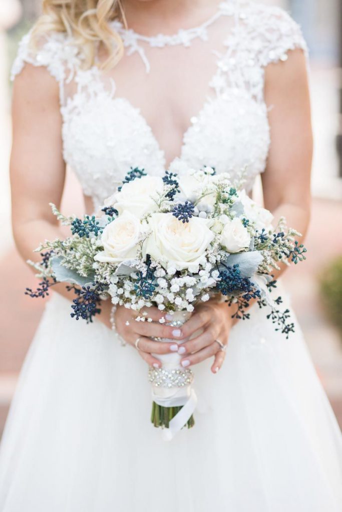 bride wearing lace wedding dress holding a bouquet with white and blue flowers