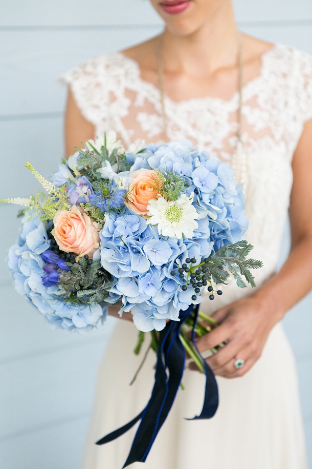 bride holding a wedding bouquet with blue hydrangeas, peach color roses and navy blue ribbon