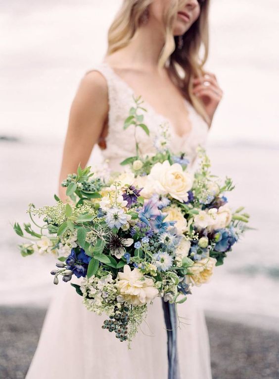 bride holding a big wedding bouquet with white, greenery and blue colors