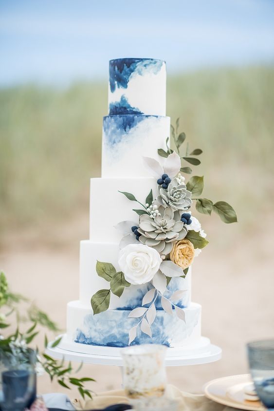5 tiered wedding cake with white frosting and blue watercolor, toped with flowers