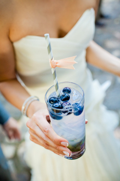 bride holding a glass of drink with striped straw and blueberries