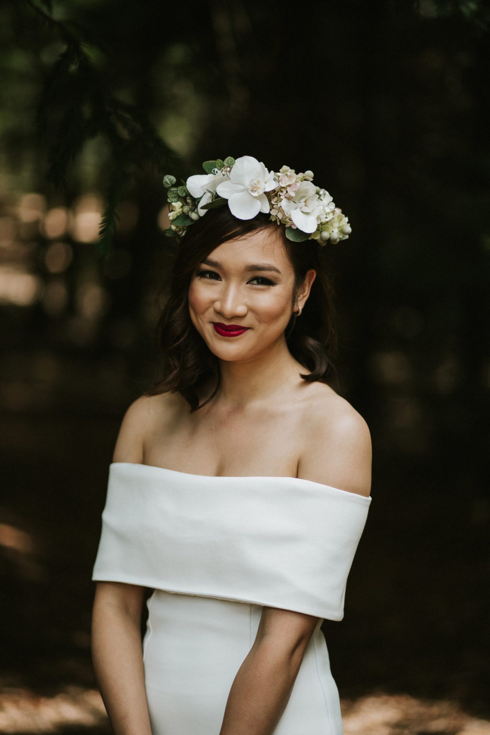 bride wearing off the shoulders wedding dress, red lipstick and all white flowers floral crown