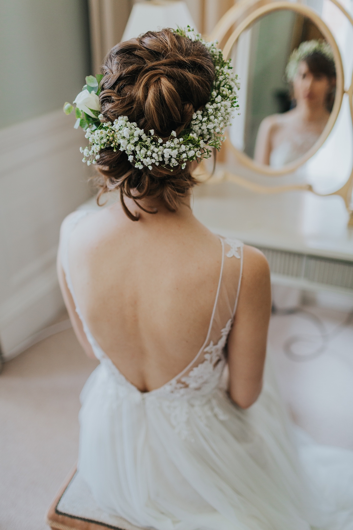 bride looking at herself in the mirror, wearing hair up and baby's breath floral crown