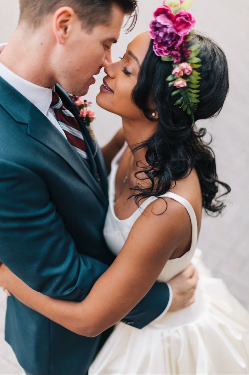 bride and groom hugging, about to kiss. groom wears navy blue suit and bride wears her hair down with a beautiful floral piece