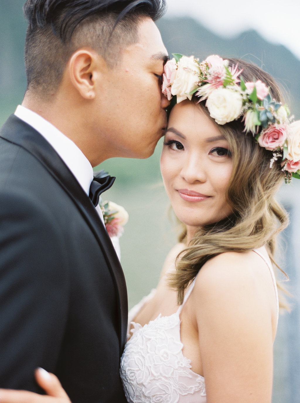 bride and groom portrait. groom kisses bride on the forehead. bride wears hair down topped with a floral crown