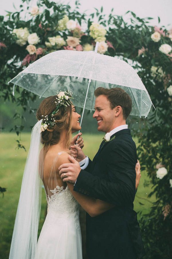 bride and groom posing under an umbrella on the rain