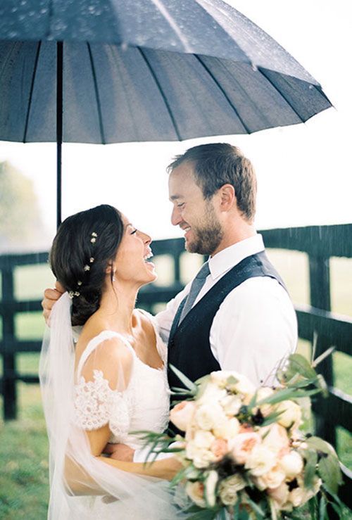 portrait of a bride and groom looking at each other and smiling under an umbrella on a rainy day wedding