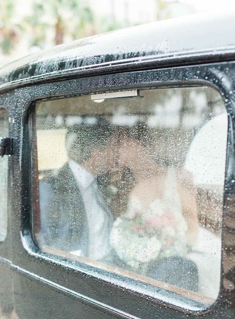 portrait of a bride and groom kissing inside their getaway car wet from the rain