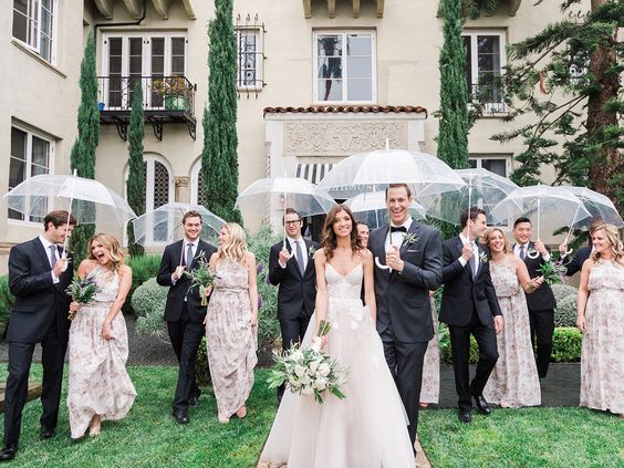 bride and groom holding matching clear umbrellas with their wedding party on a rainy day wedding