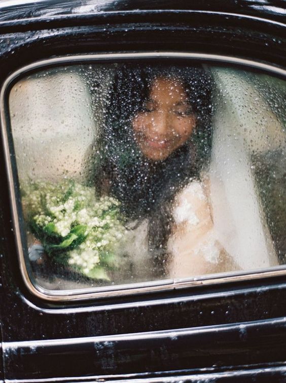 portrait of a bride holding her bouquet inside the car with the window wet from the rain