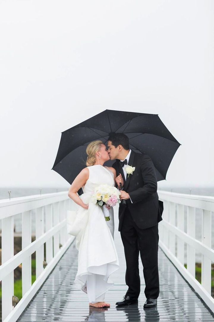 bride and groom kissing under an umbrella on a rainy wedding day
