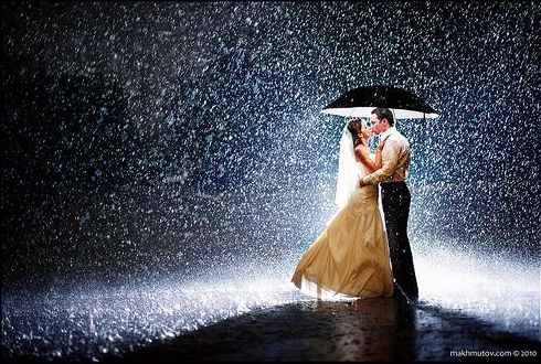 bride and groom kissing under an umbrella on a rainy night