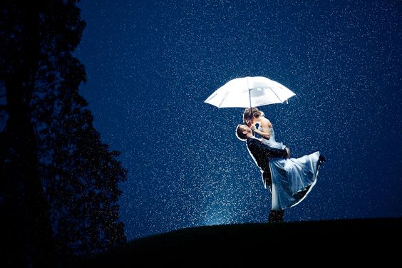 groom lifting up the bride and kissing under an umbrella on a rainy night