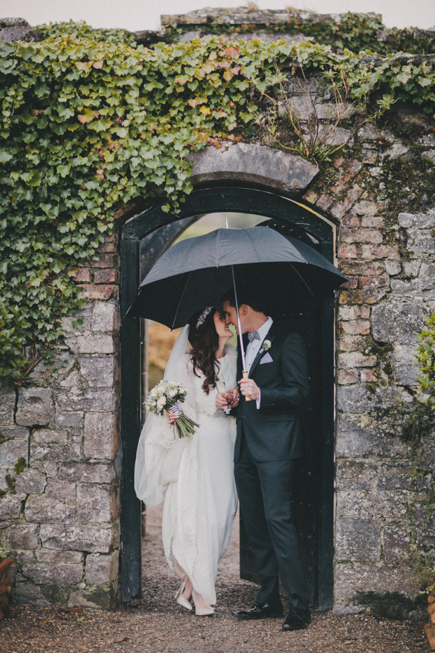bride and groom kissing under an umbrella on a rainy day wedding