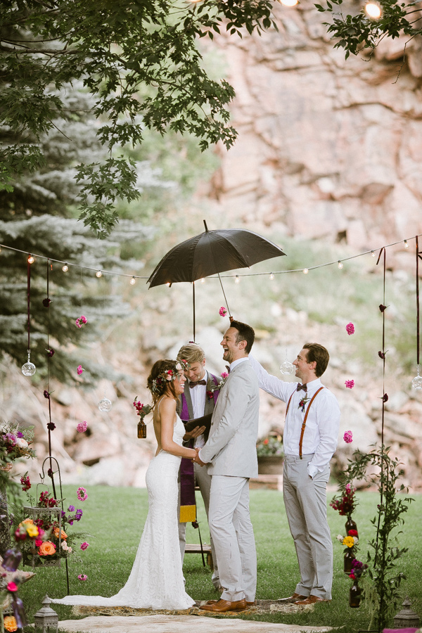 bride and groom holding hands during ceremony while a groomsmen holds an umbrella