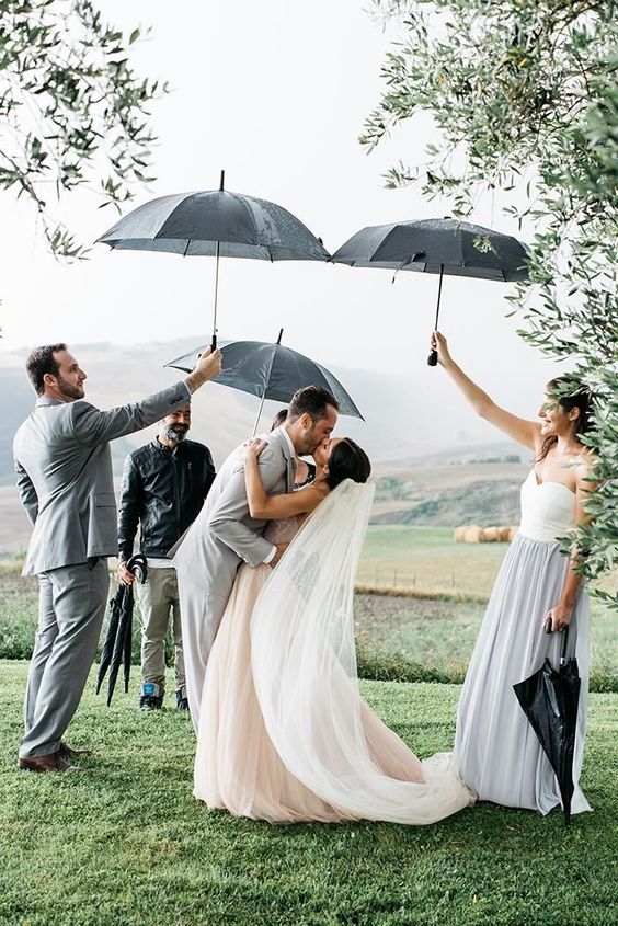 bride and groom kissing after wedding ceremony with a groomsmen and bridesmaid holding an umbrella