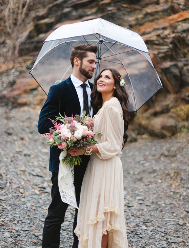 bride and groom posing under a clear umbrella on a rainy day